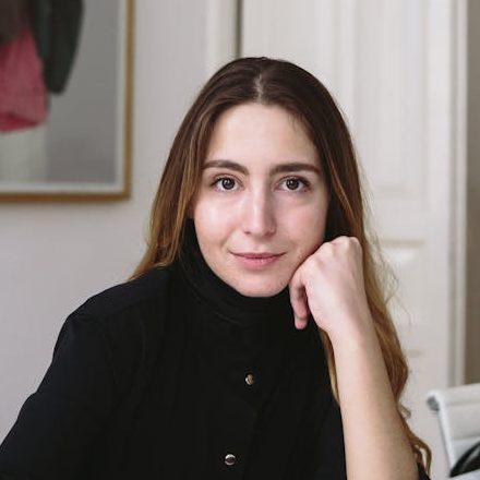 Portrait of a woman in a modern office setting, seated at a desk with a laptop.